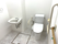 トイレには手すりが複数箇所に取りつけられている。壁にペーパーホルダーと緑色の緊急通報装置が設置されている。
