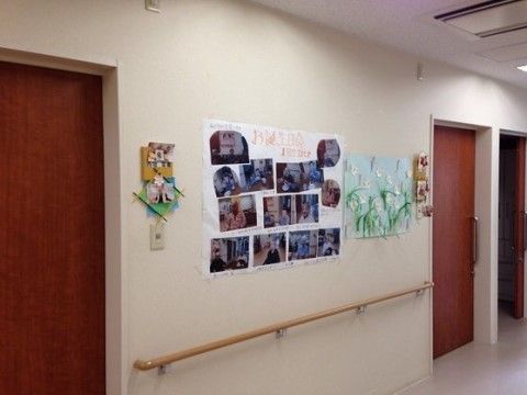 居室へのドアの間の壁に、写真が飾られた模造紙が貼られた廊下