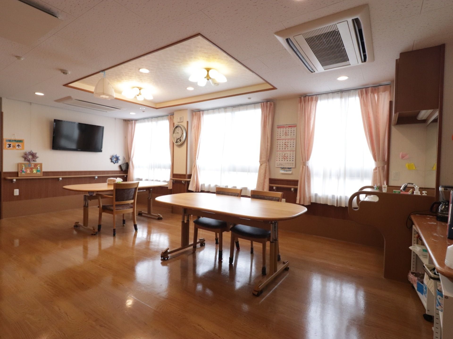 楕円形のテーブルや薄桃色のカーテンを使用することで、優しい空間となっている。穏やかな気持ちで過ごせる共有スペースである。