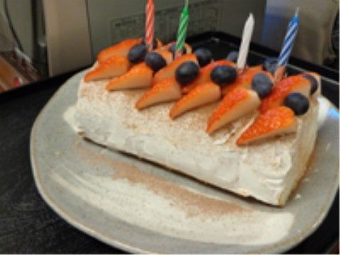 イチゴとブルーベリーが盛りつけられ、ろうそくが刺さった四角いケーキ