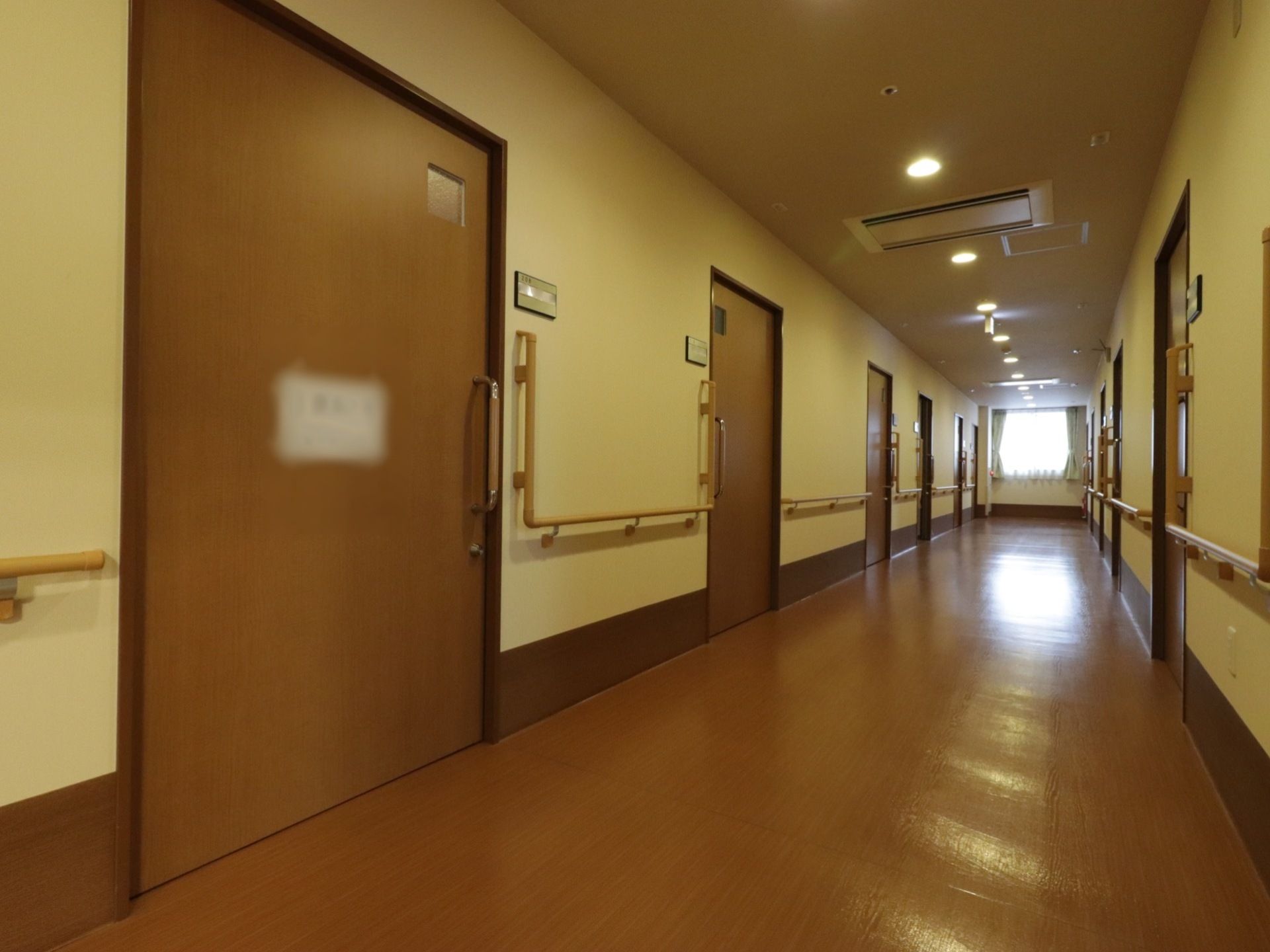 長く伸びた通路の両側には居室が並んでいる。入口扉は広く、手すりも壁に設置されていて、歩行に不安のある方も安心して移動できる。