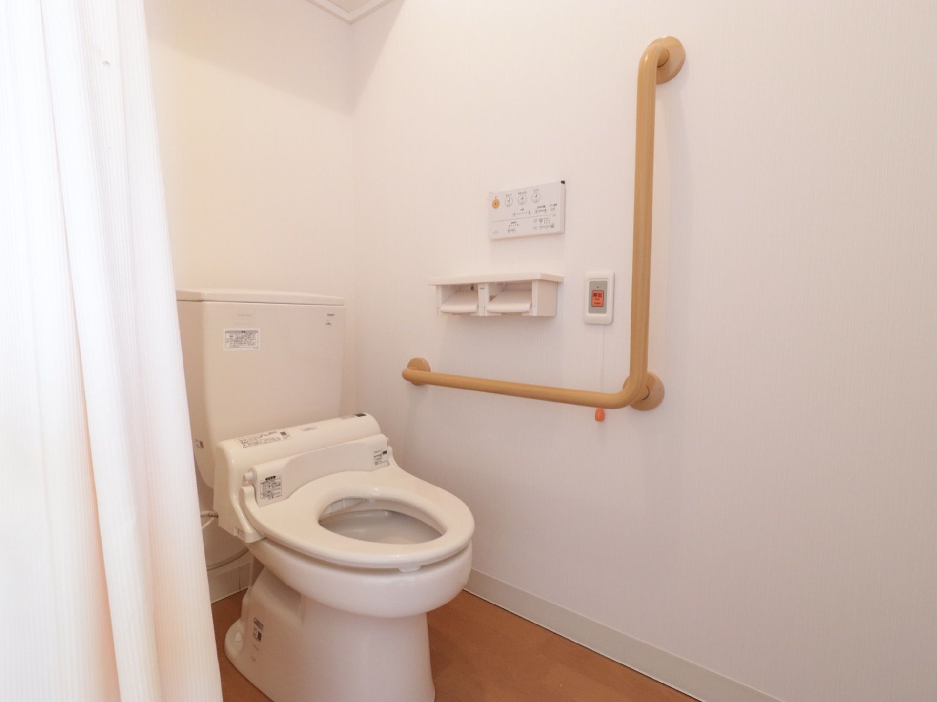 トイレは広く、カーテンの仕切りがある。壁にはL字型の手すりが付いており、呼び出しボタンも設置されている。