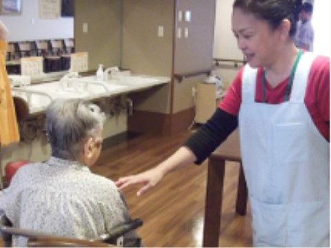 椅子に座った女性入居者様に声を掛けるエプロン姿のスタッフ