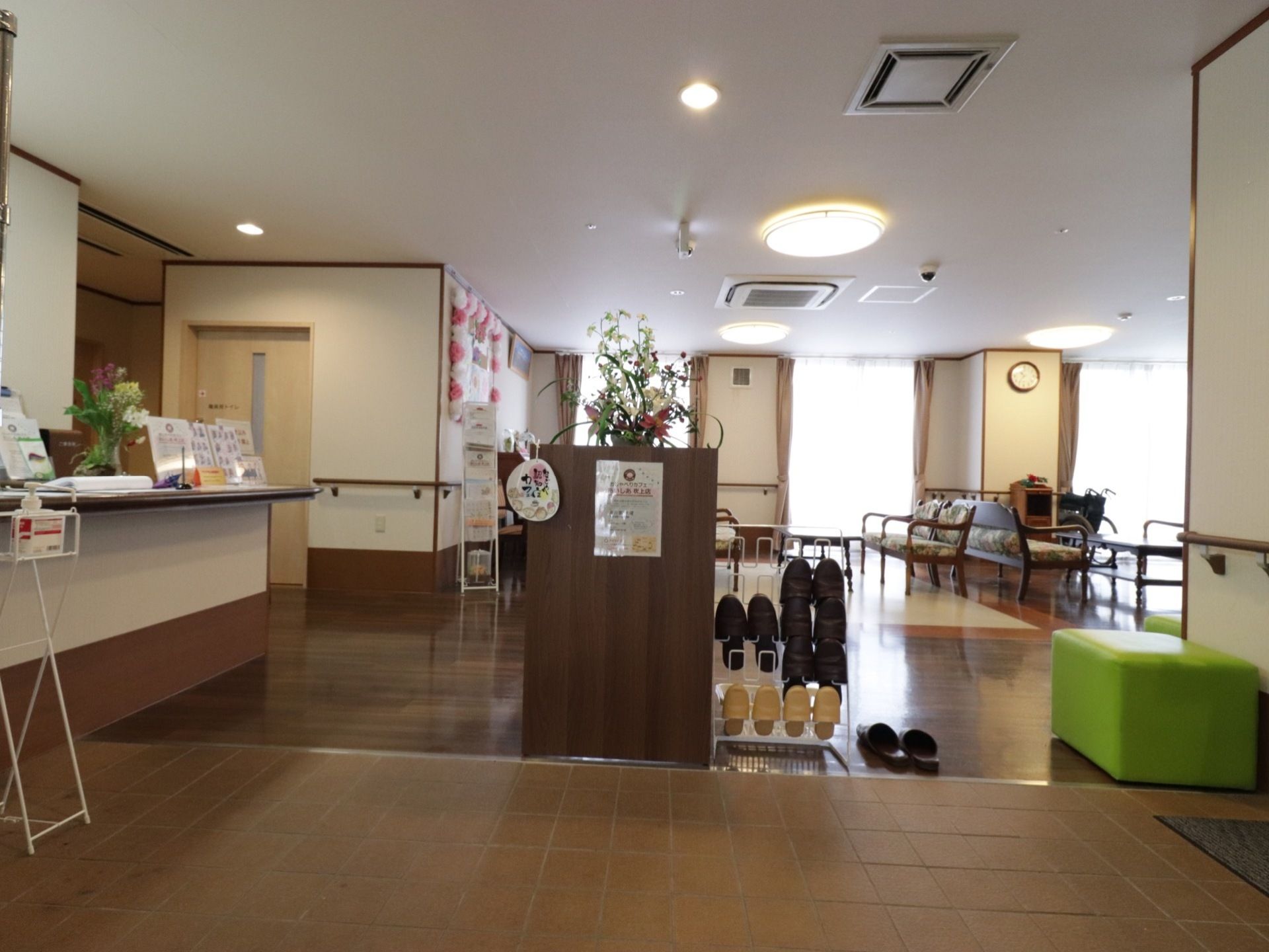玄関は広々としている。スリッパラックには6足のスリッパが収納されている。近くには緑色の椅子が置かれている。
