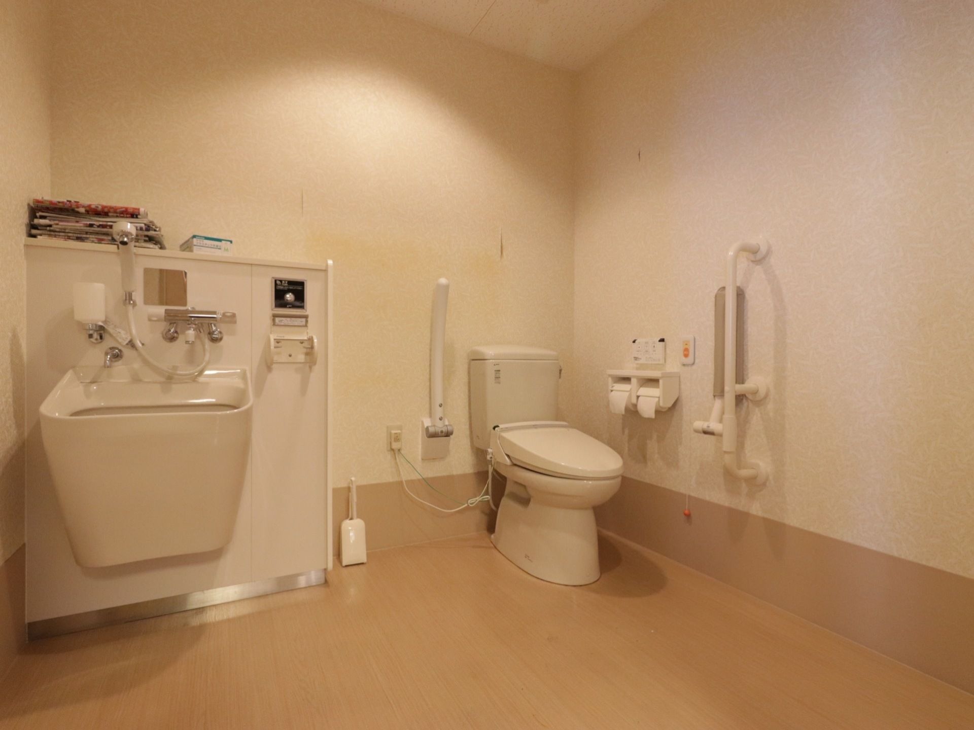 トイレには洋式便器が設置されている。便器の片側には可動式の肘置きがある。壁側にはトイレットペーパー、呼び出しボタンがある。