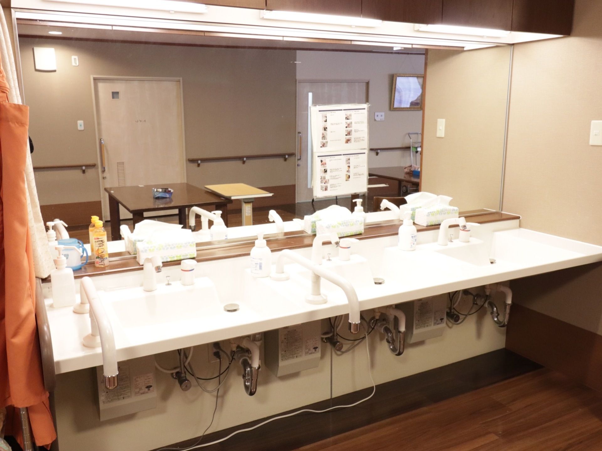 前方が鏡張りになっている。洗面台が3つ設置されている。うち1つには手すりが取り付けられていて、少し広く作られている。
