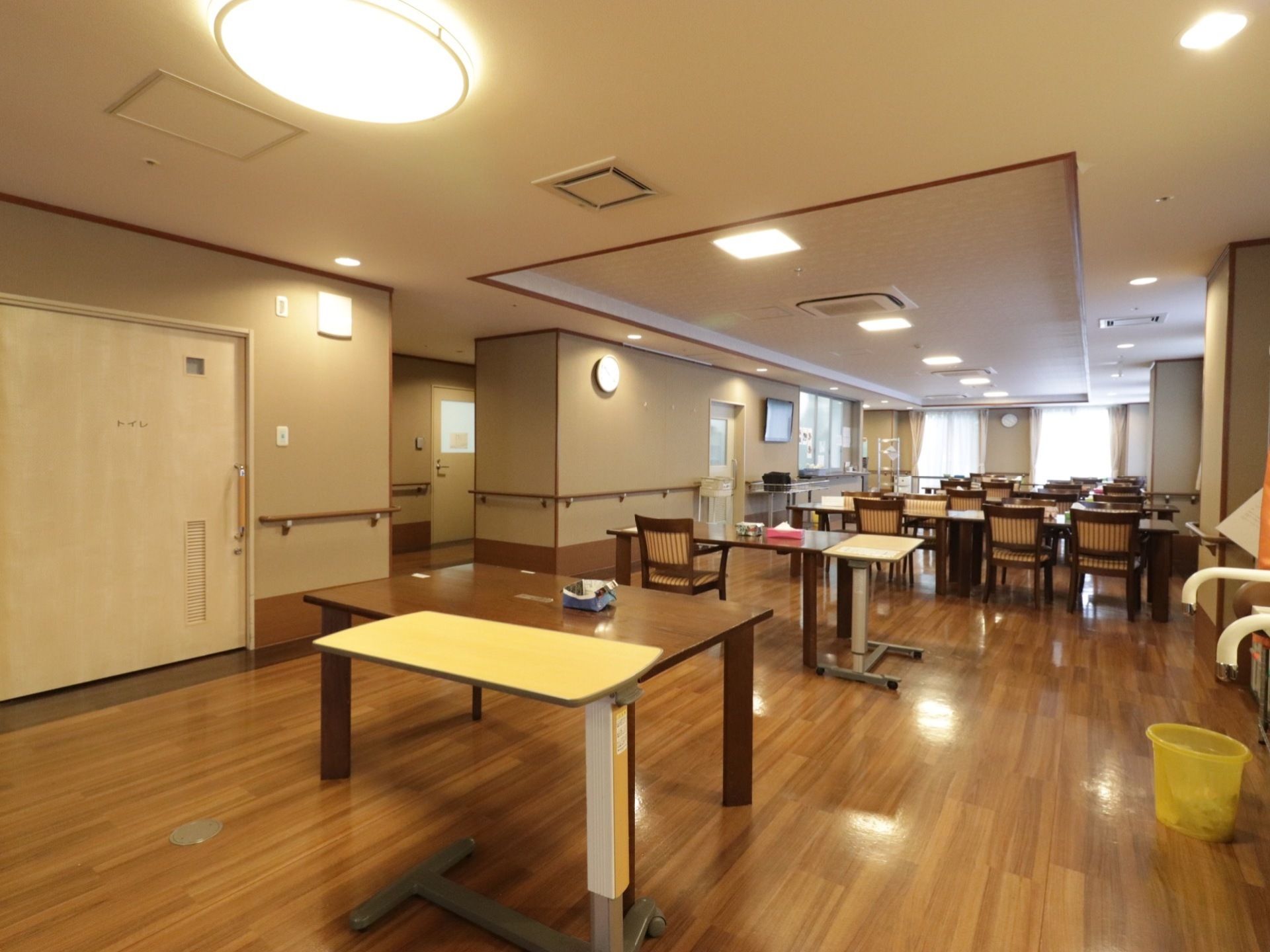 食堂には沢山のテーブルと椅子が並べられている。壁側には手すりが取り付けられている。トイレと書かれた扉もある。
