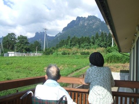 ベランダから施設周囲に広がる木々や高い山を眺める入居者様