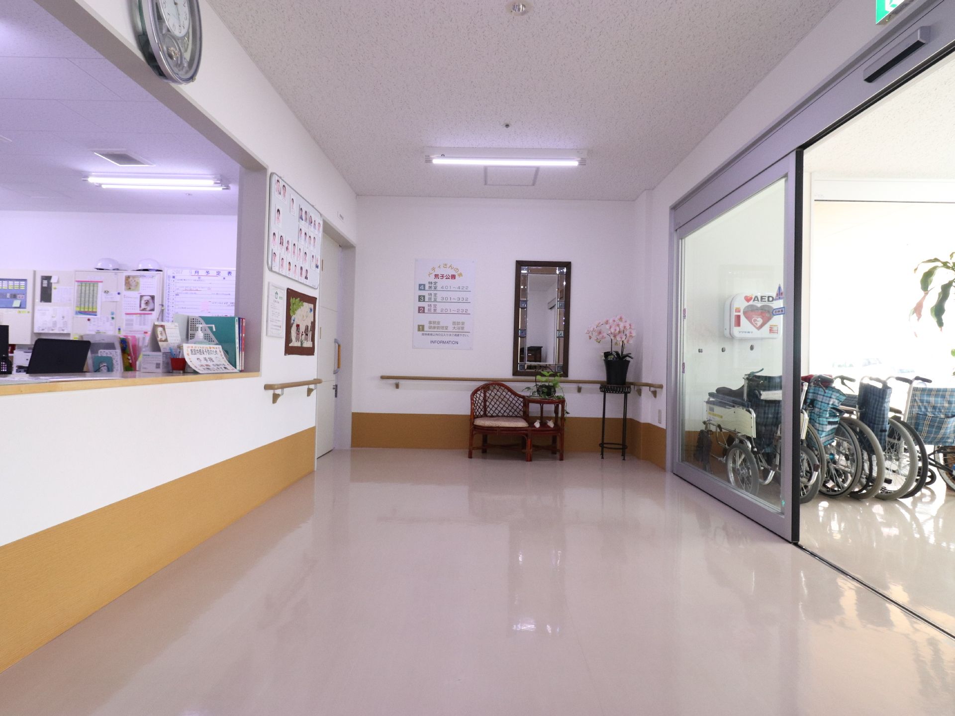 広々とした玄関ホールである。壁際には、台に置かれた胡蝶蘭の鉢やお洒落なベンチが配置されている。手すりが壁に設置されている。