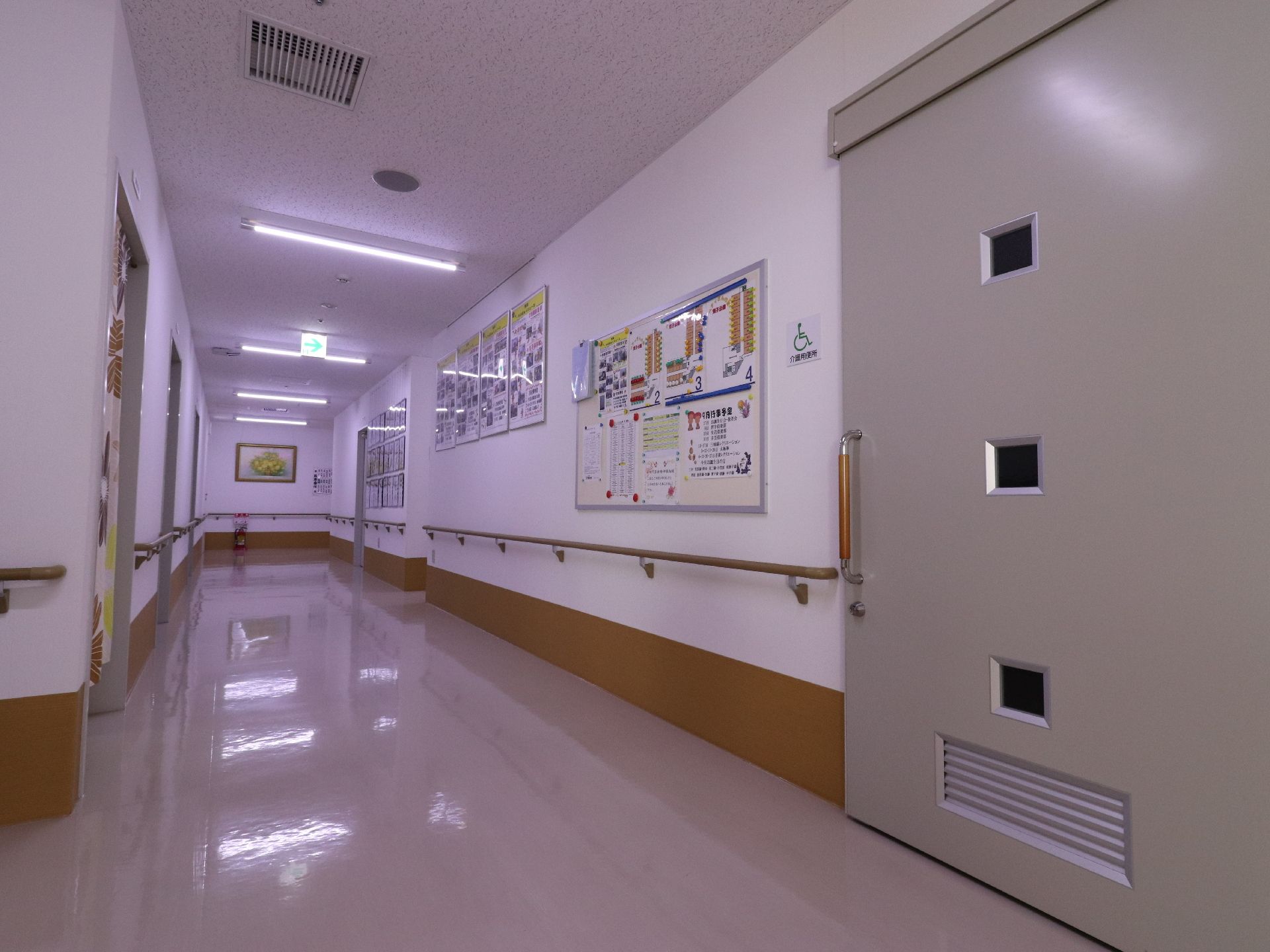 明るく広さが確保された廊下である。壁に沿って手すりが設置されている。様々なポスターや絵が飾られている。