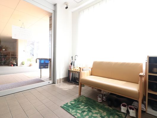 3人が座れるソファがあり、その足元には何足かの靴が置かれている。奥の壁際には傘立てがあり、傘がささっている。"