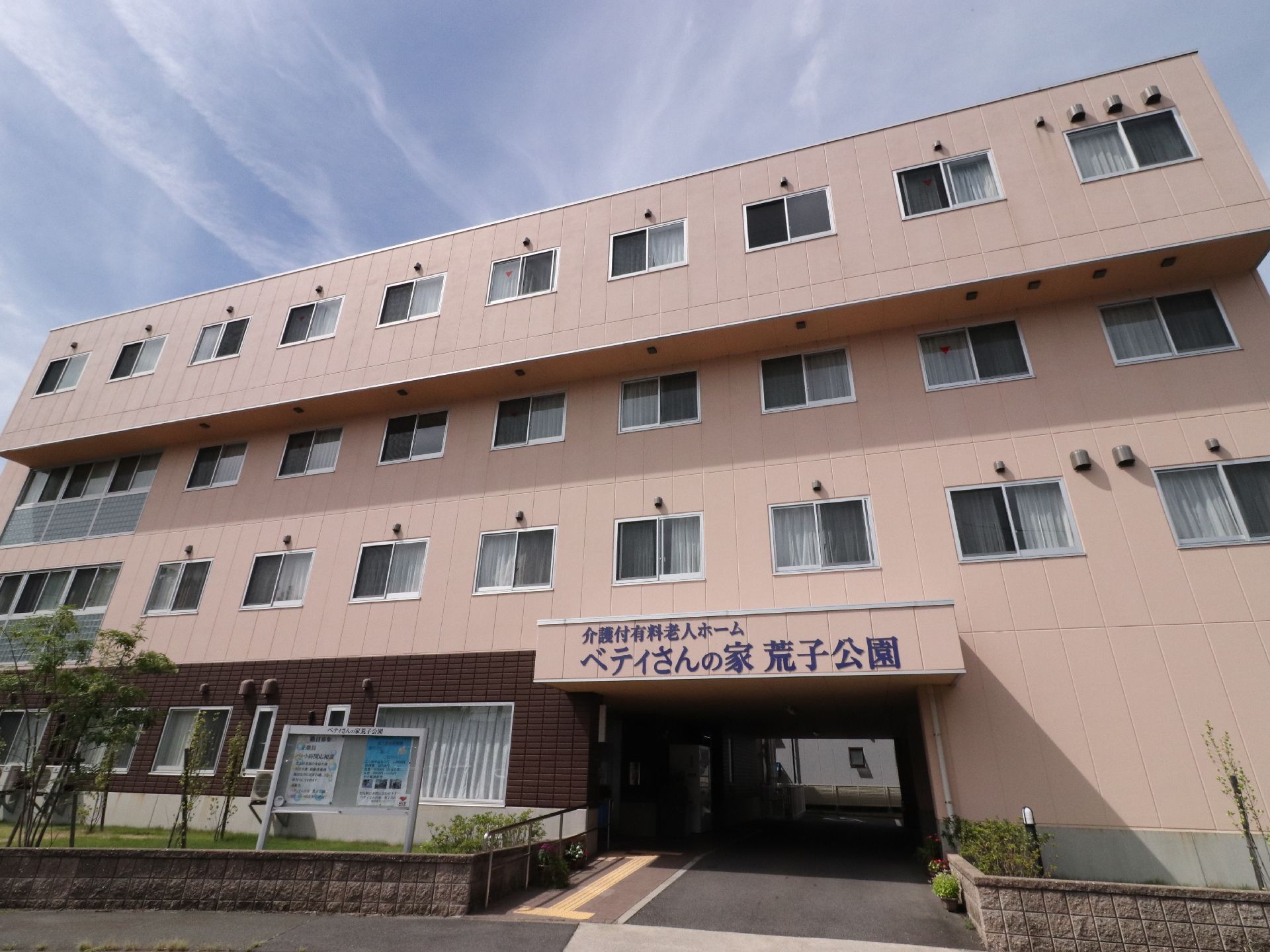 4階建てとなっている施設外観は個室の窓が非常に多くある。正面入り口付近には、青色で書かれた施設名の看板が掲げられている。