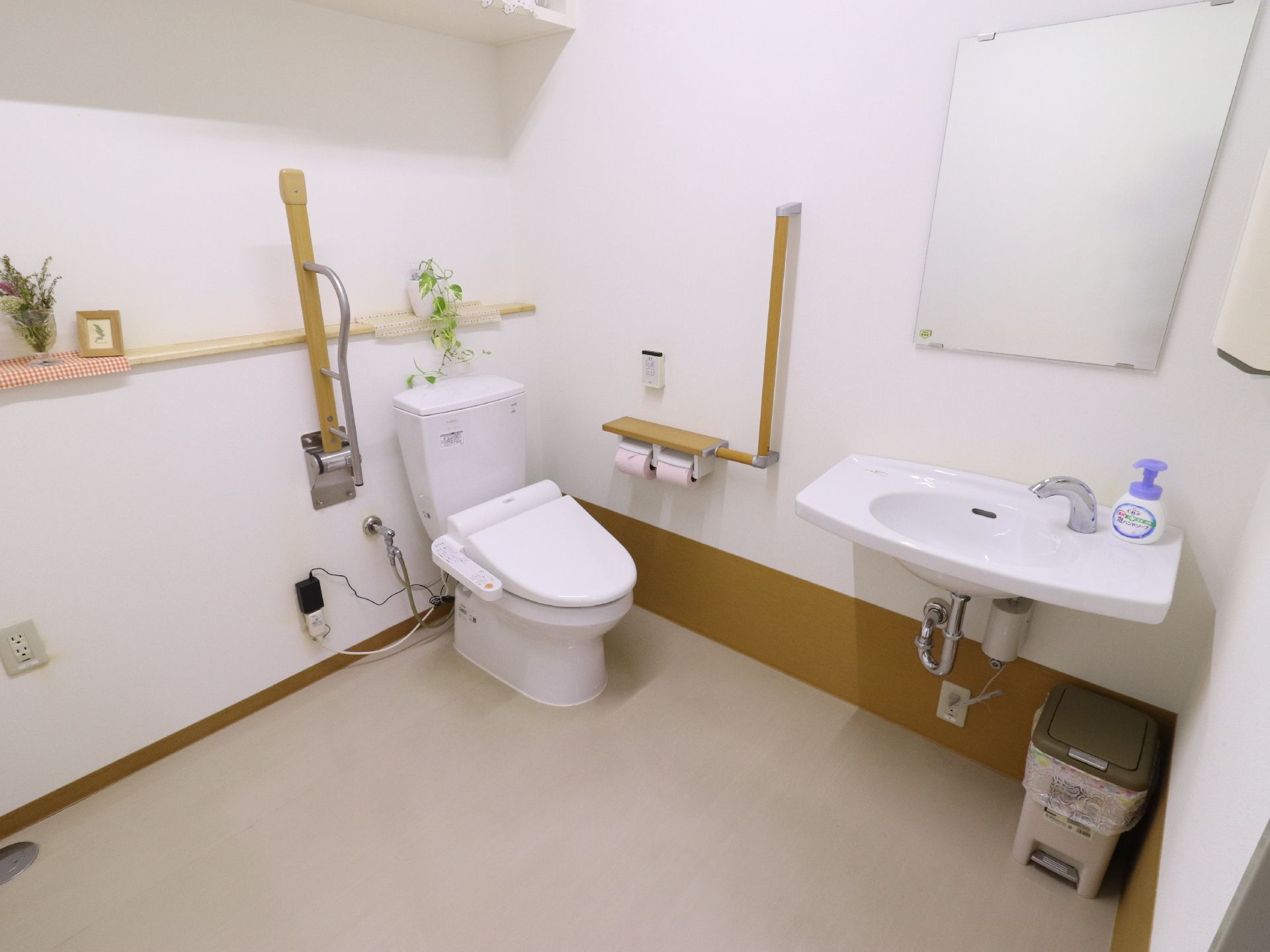 スペースの広く取られているトイレルームは、壁際に洋式便器があり、周りには手すりが取り付けられている。手洗い場にはハンドソープが置かれている。