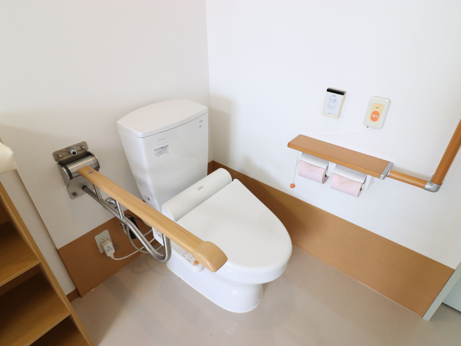 トイレルームにはフタが閉じた状態の便座があり、両サイドに手すり、壁にはスタッフ呼び出し用のブザーが設置されている。
