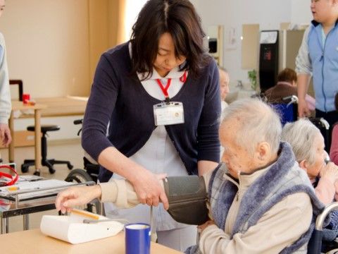 椅子に座った男性入居者様の腕に血圧計を取り付けているスタッフ