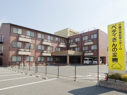 ブラウンのエル型構造の外観である。敷地内は広々としたスペースを設け、駐車場を備えている。黄色の施設の旗を掲げている。