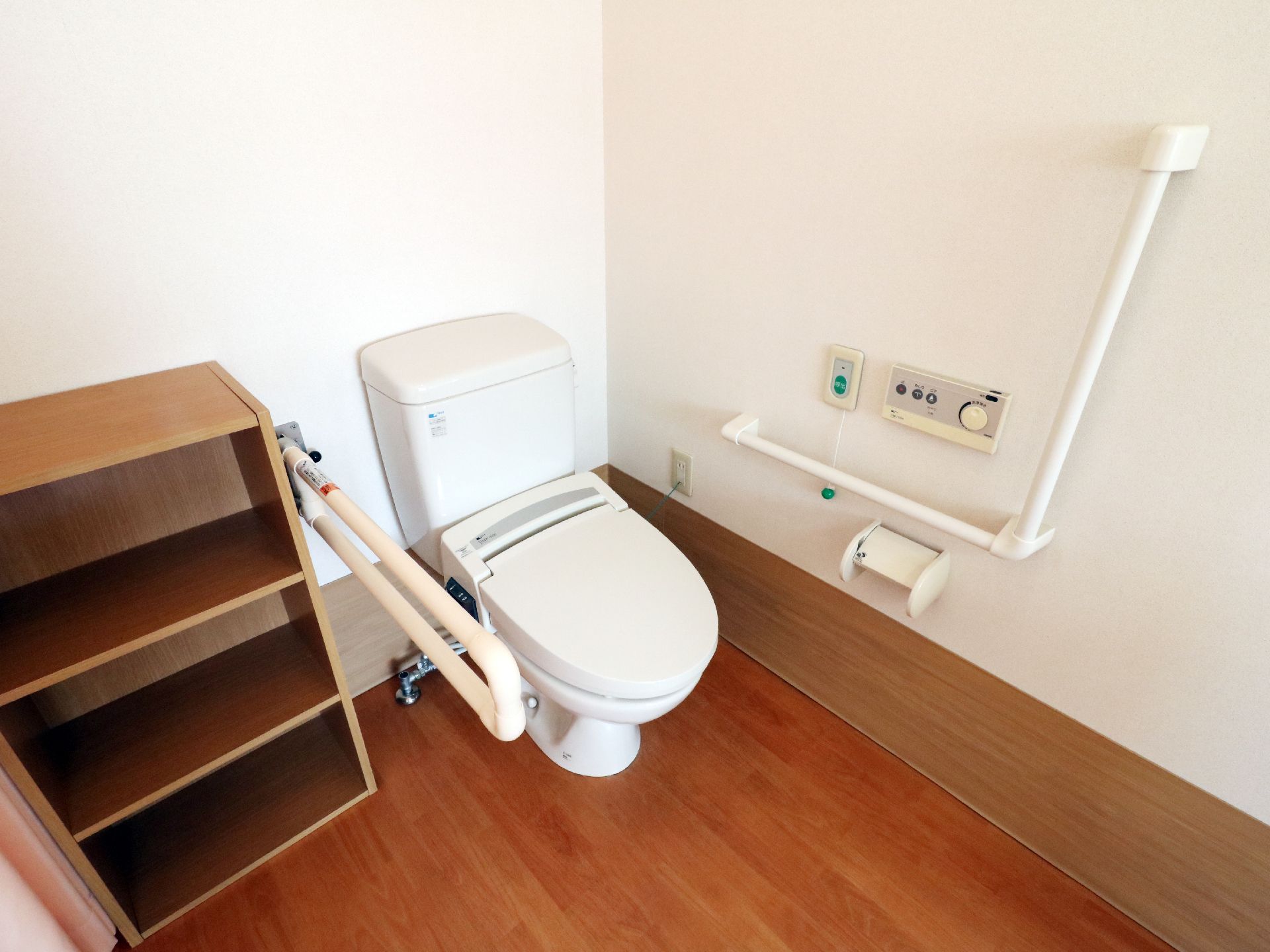 洋式トイレの両側には手すりが設置されています。座って左側の壁にはナースコールがあり、その横には操作パネルがあります。