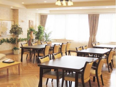 壁一面に窓があり、光がたっぷりと射し込む明るい雰囲気の部屋。木製のテーブルと菜の花色の椅子が設置されている。