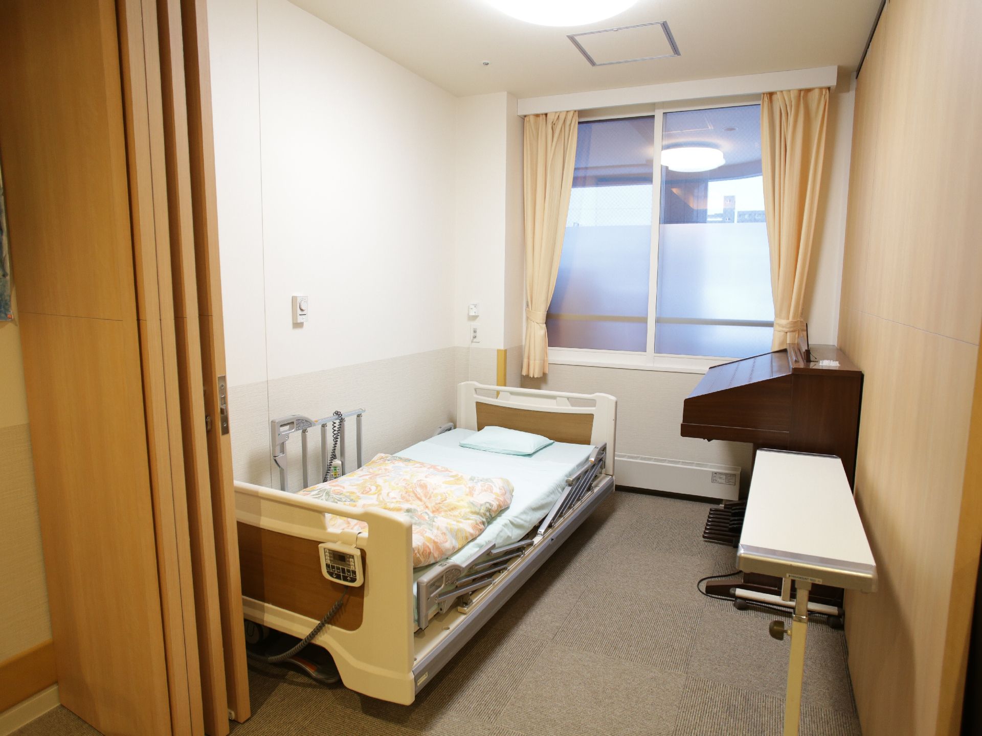 窓が付いた個室には、電動ベッドが設置されています。緊急時にスタッフをよびだすことができるボタンも壁に設置されています。