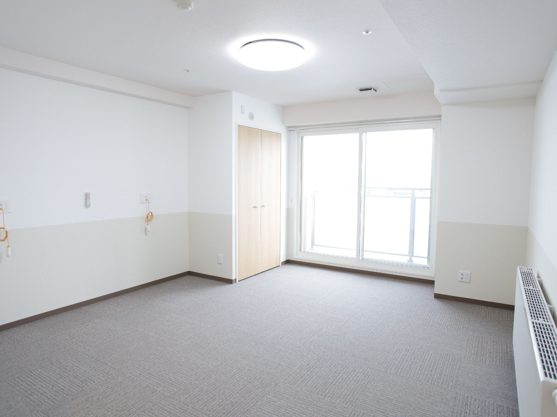 白を基調とした個室。大きな掃き出し窓の外側にはフェンスが設置されています。両開きのクローゼットがあり、床はフラットです。