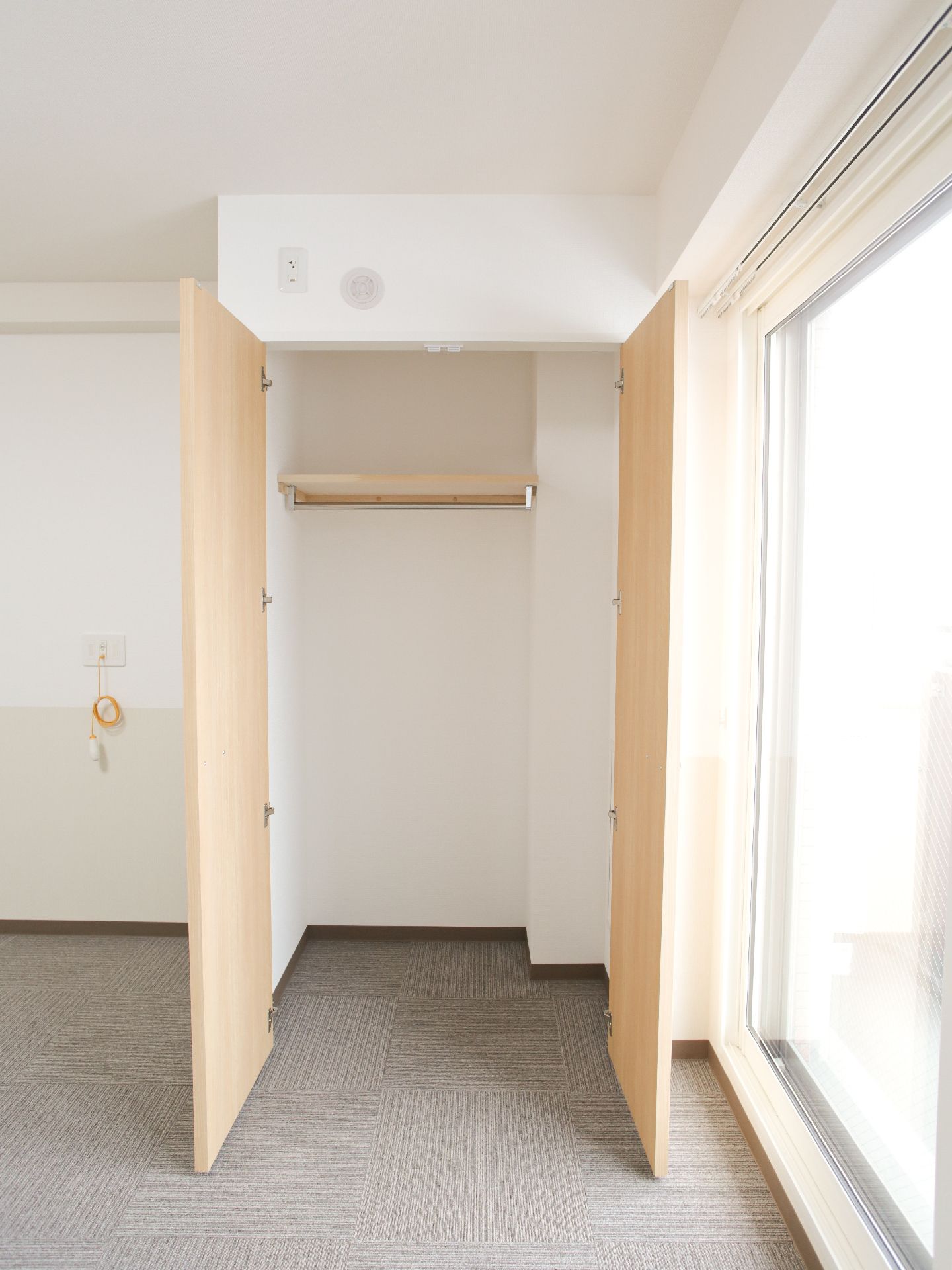 個室の角部分に設置されたクローゼットです。2枚の扉は左右に大きく開きます。内部は上部に棚が設けられ、ハンガーが掛けられるバーがあります。