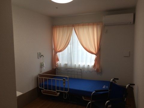 オレンジのカーテンが掛けられた窓の前にベッドがある部屋