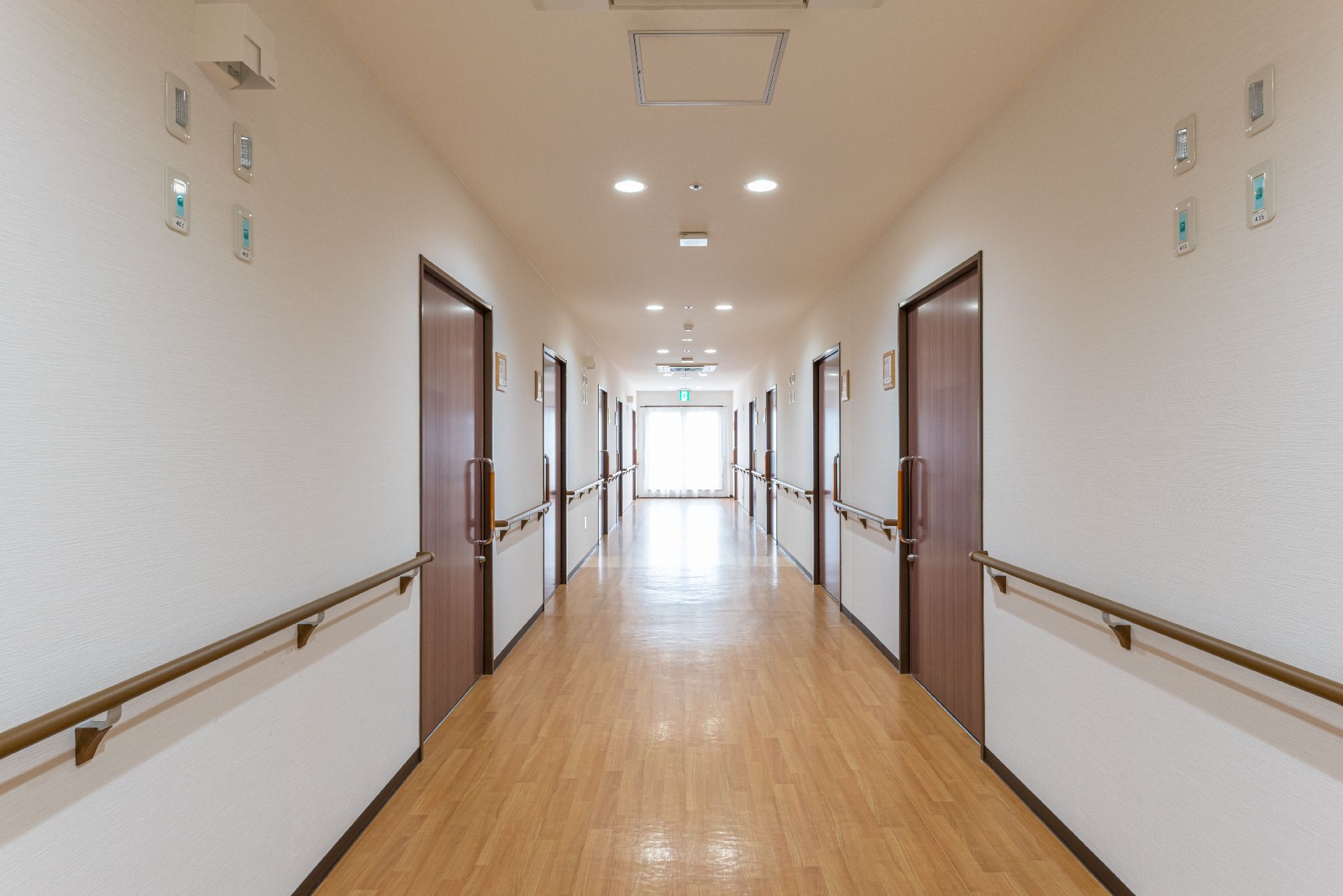 幅の広いまっすぐな廊下は両サイドに手すりと居室のドアがあり突き当りには大きな窓がある。