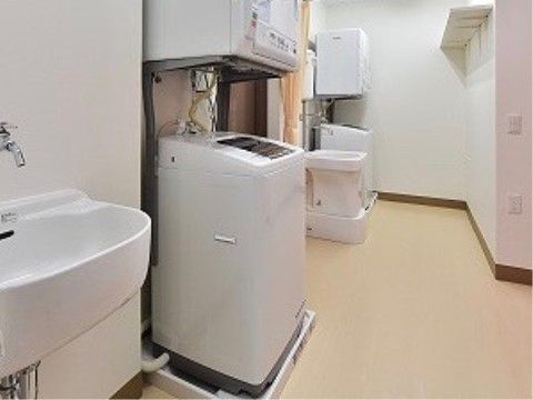 洗濯室には、２台の乾燥機付き洗濯機が設置されている。仕切りカーテンが利用できるようになっており、洗い場も設けられている。