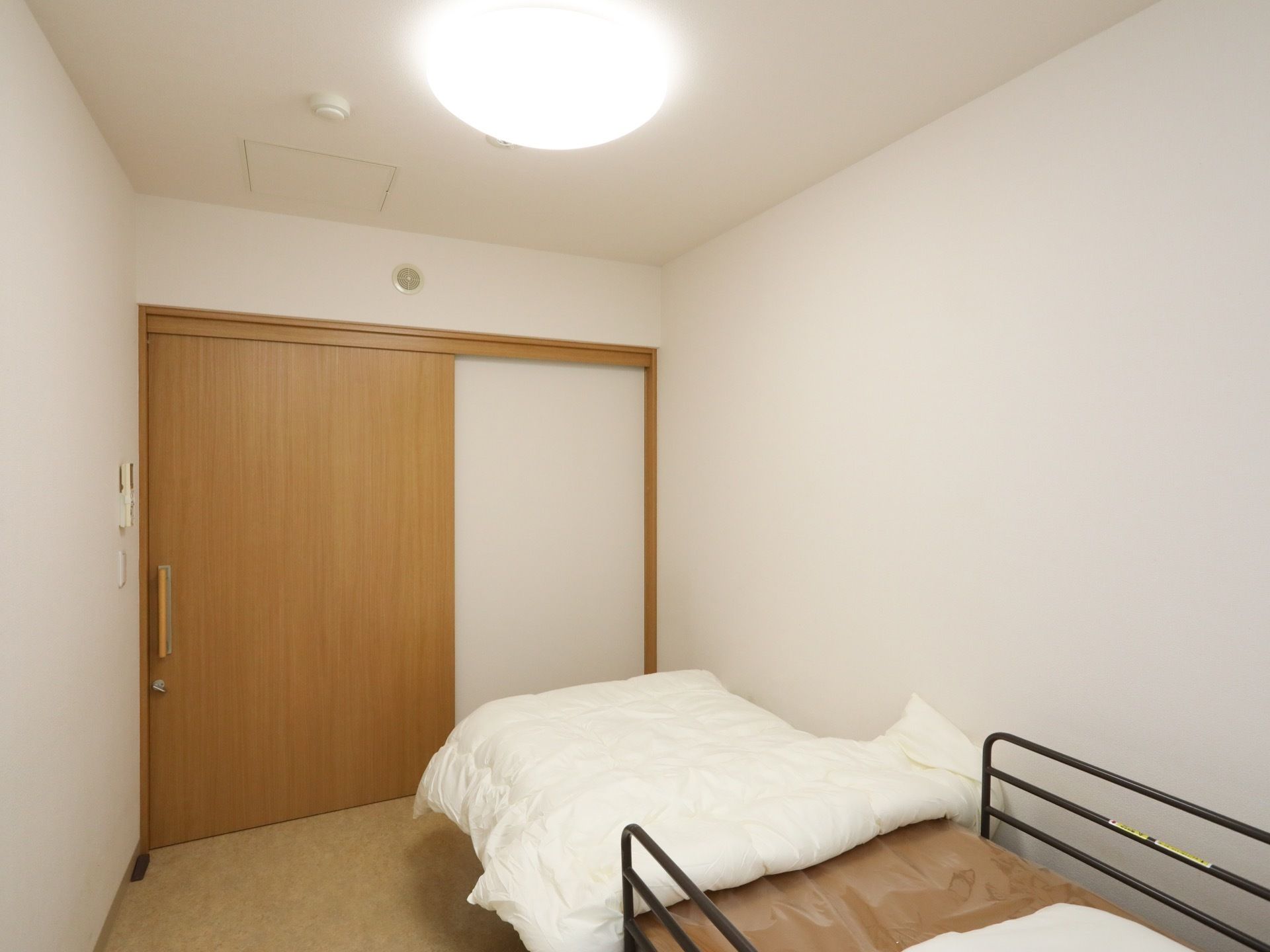 白い壁が清潔感をかもし出している居室。LEDライトが部屋を明るく照らしている。介護用ベッドの両側には柵がある。