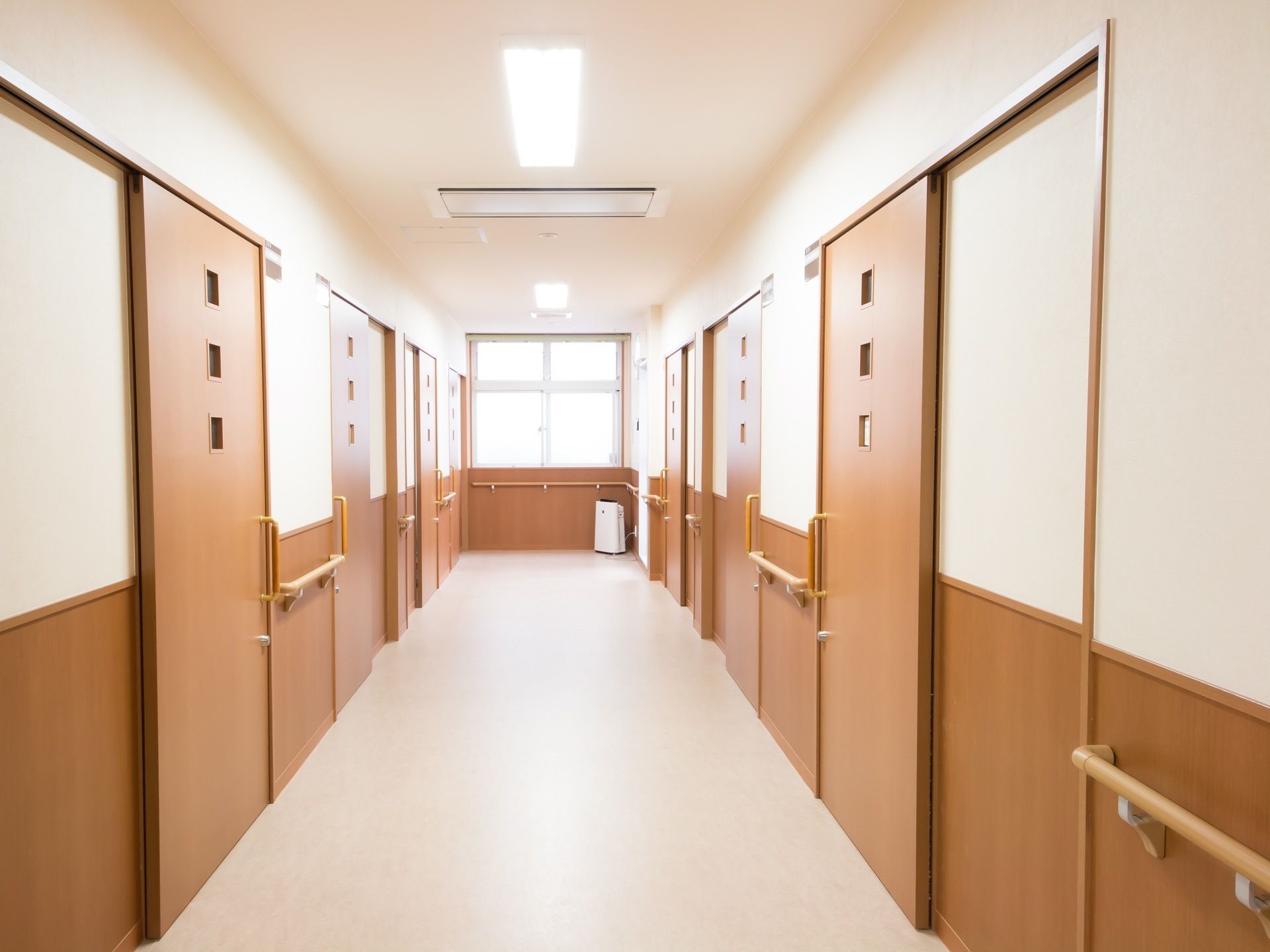 広々とした廊下の両側に居室が並んでいる。扉は木製で、すべてスライドドアになっている。壁には手すりがついている。