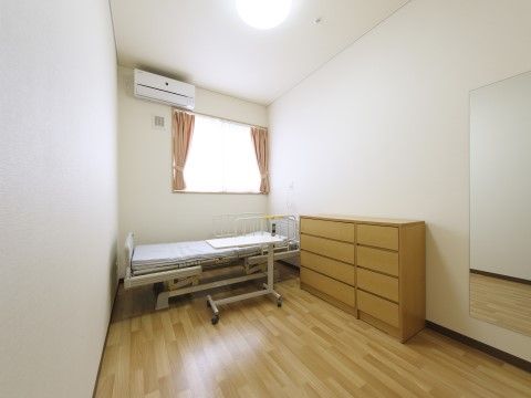 窓の前にリクライニングする介護用ベッドが置かれている居室