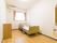 奥に長い部屋である。腰高窓にピンクのカーテンがかかっている。窓の上部にエアコンがある。壁際に手すりのあるベッドがある。