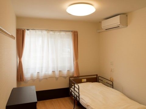 白いレースカーテンがかかった窓の前にベッドが置かれた部屋