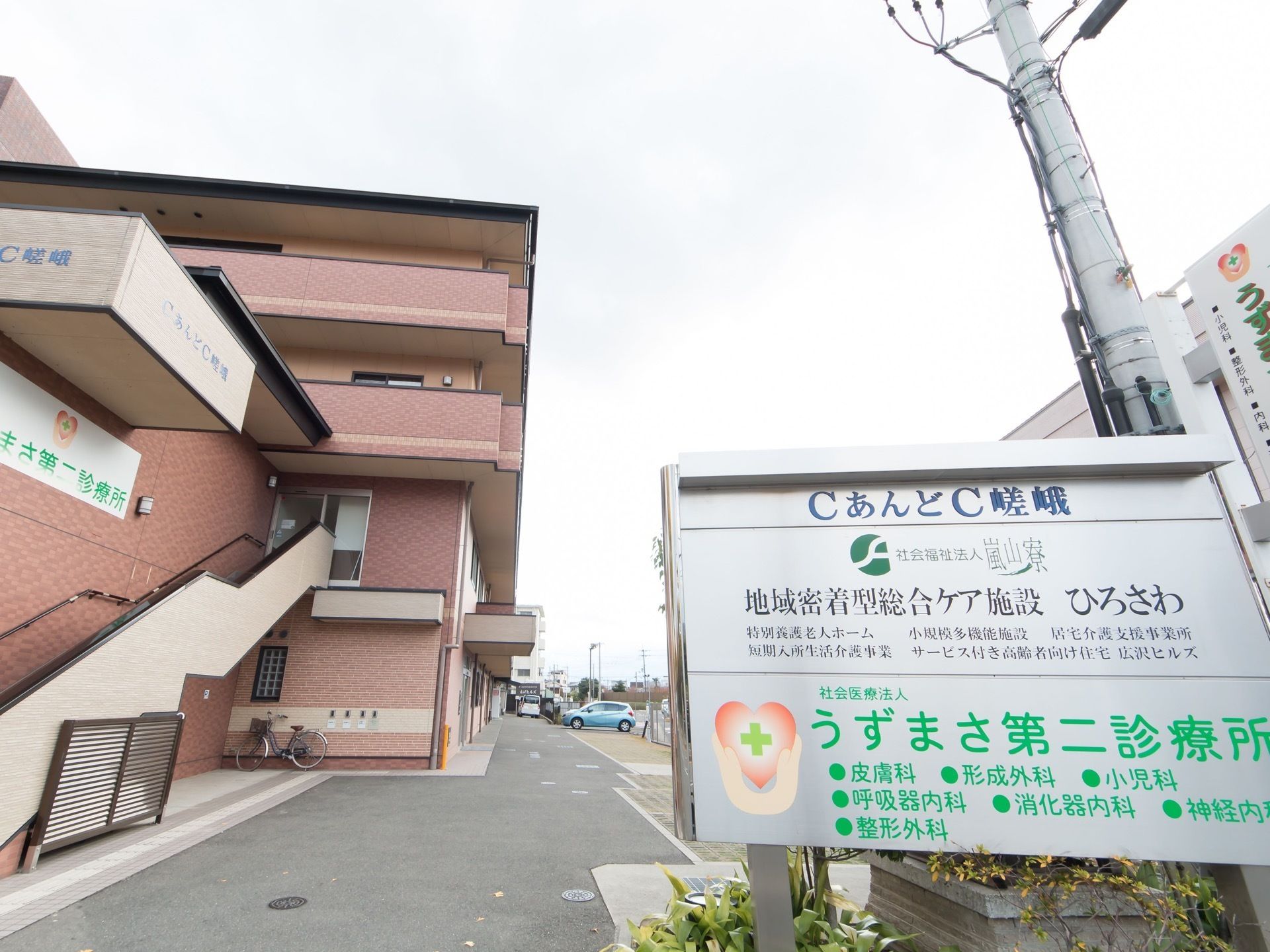 施設は４階建てでピンクがかったベージュ色の外観である。２階へと直接出入りできる外階段が設置されている。施設の看板が立てかけられている。