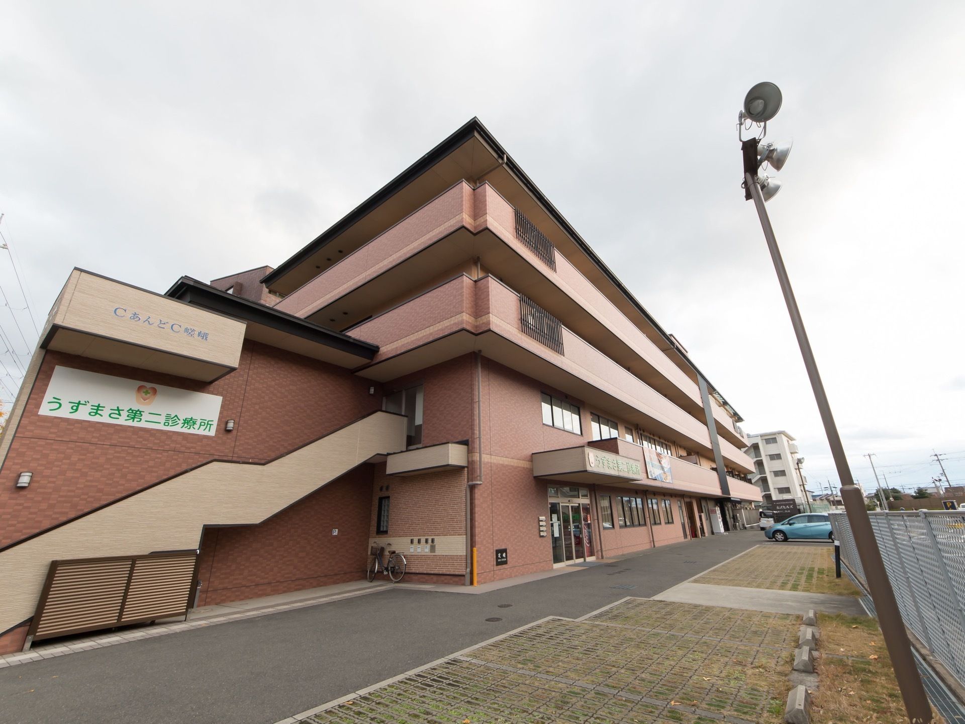 施設は４階建てで、２階部分には外階段がある。敷地内には複数の車が停められるように駐車スペースが完備されている。
