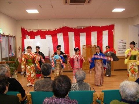 紅白の垂れ幕の前で開催されている子供たちの踊りを見学する入居者様