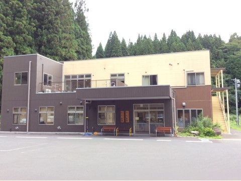 背後には針葉樹の森があり、一部平屋の２階建で外壁は茶色とベージュに塗られている。玄関の上にはひさしがあり、両脇にはベンチが置いてある。