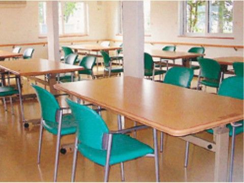 ２方向に窓があり、明るい光が差し込んでいる。壁際には手すりがあり、移動が楽に行える。テーブルと椅子がゆったり配置されている。