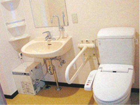 洗面台が備え付けられたトイレである。個室の角には収納棚が取り付けられている。温水洗浄機能付きの便座となっている。