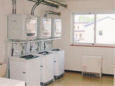 白を基調とした清潔感のある空間である。室内には窓が設置されており、乾燥機と洗濯機が３台並んで置かれている。