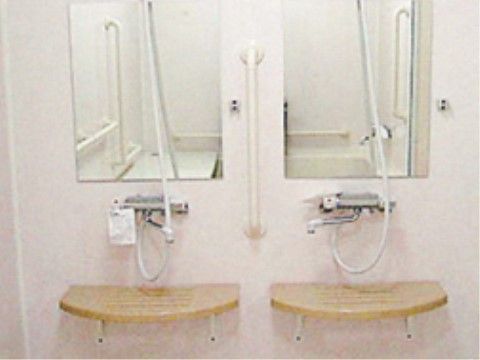 白い壁にシャワーや四角い鏡、木製のテーブルが２組ずつ取り付けられている。間には、手すりが設置されている。