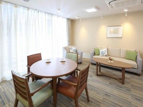 木の床の部屋に、テーブルと数人がけのソファや椅子が置かれている。天井をはじめ、壁の上部に複数の間接照明がついている。