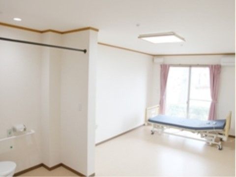 青いマットレスの介護用ベッドが窓の前に置かれている居室