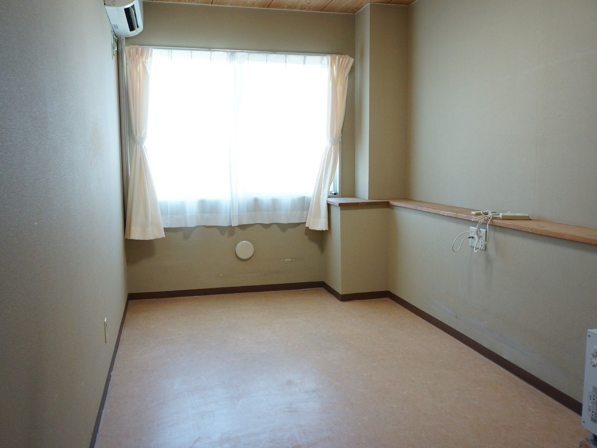 入居者の個室の床は薄い黄色っぽい色になっている。カーテンが取り付けられている窓からは自然光が入ってきている。