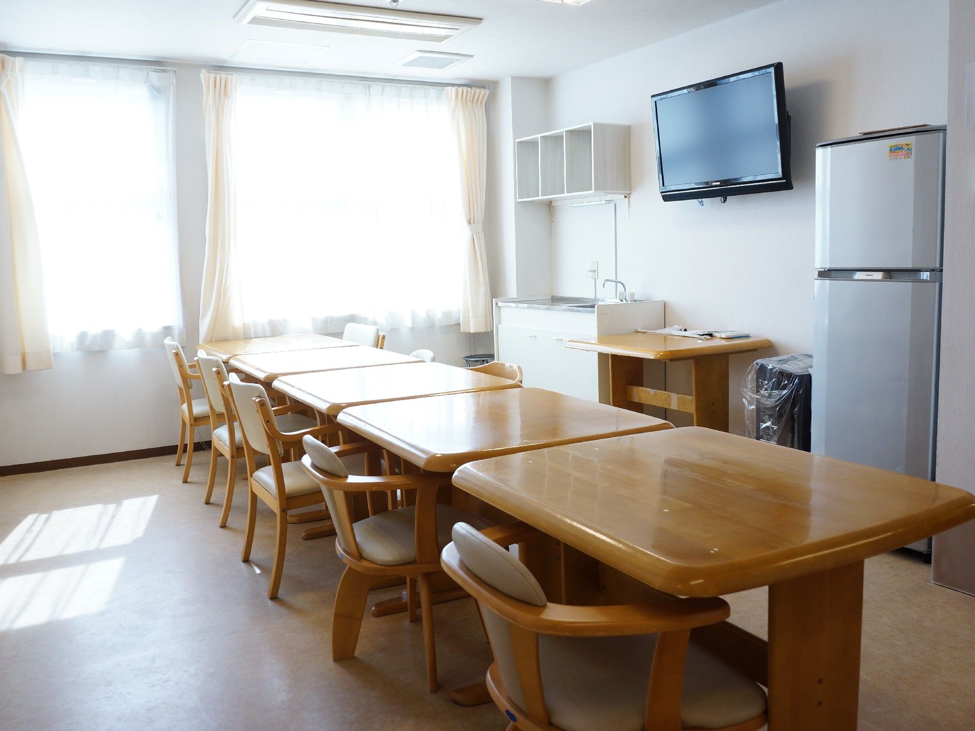 テレビが壁に設置された広いリビング。冷蔵庫も設置され、ダイニングとしても使用される。