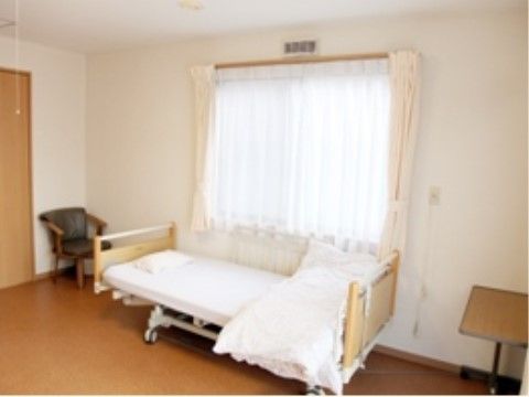 窓の前に布団が畳まれた介護用ベッドが置かれている居室