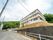 施設は、坂を上った先の高台にある３階建ての建物である。側には広い駐車場があり、建物の背後は木が茂った森になっている。