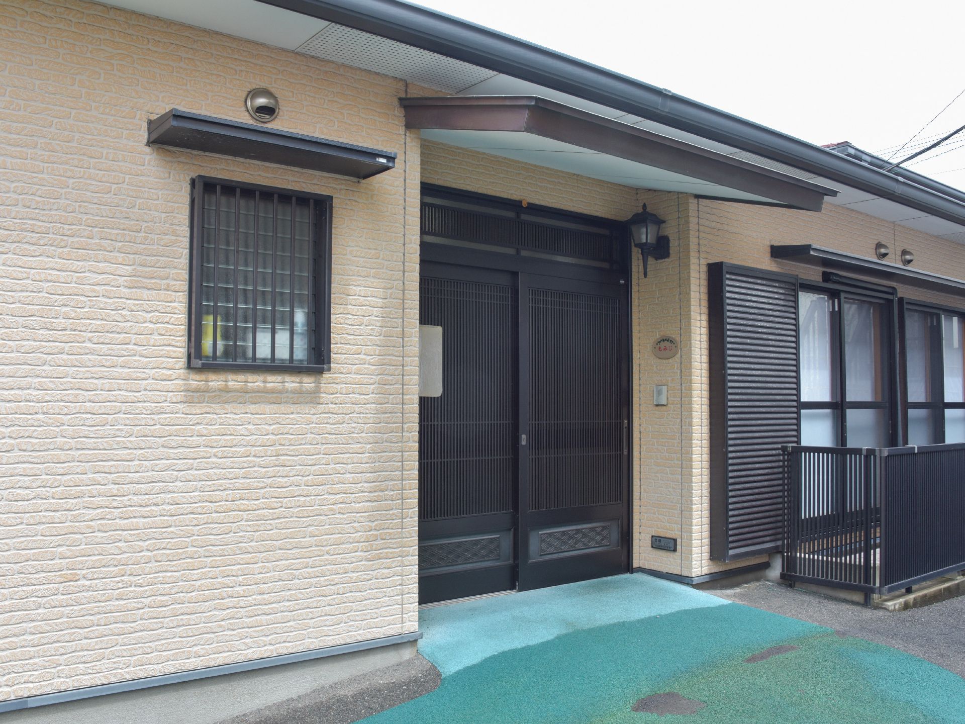 一般の住宅のような作りの施設。玄関はスライド式のドアでベランダもみえる。入り口まではグリーンの敷物がしてある。