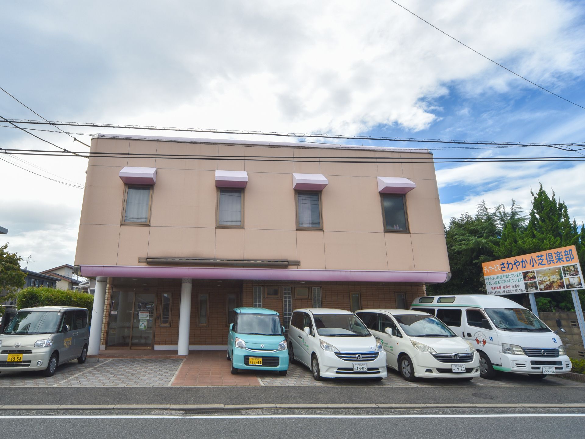 2階建ての明るい外壁の施設外観である。メイン道路からのアクセスも良く、車両を用意に進入させることが出来る。