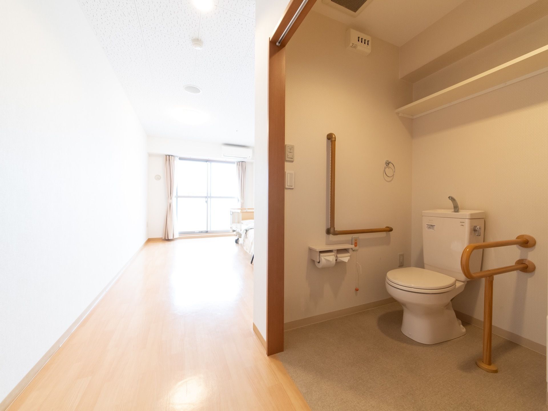 居室に備えた広々としたトイレスペースである。便座は出入口の正面に設置され、両側に手すりを備えている。上部に棚を設けている。